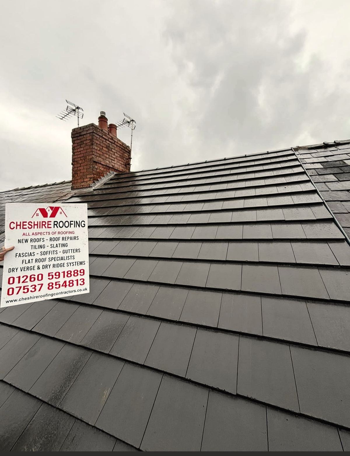Completed slate roof with Cheshire Roofing Contractors signboard showing services and phone numbers 01260 591889 and 07537 854813